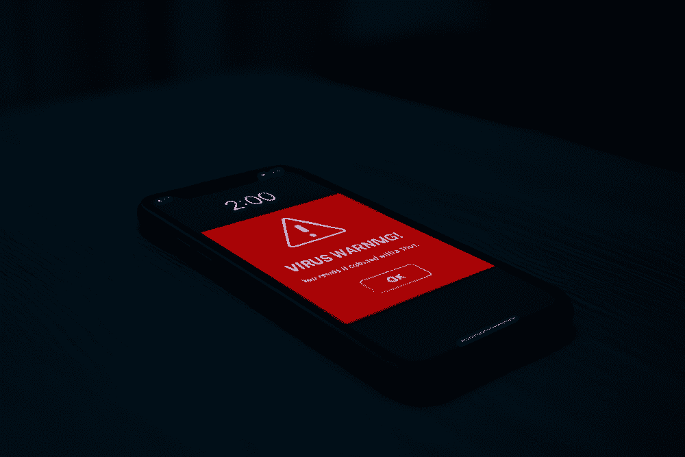 深夜の暗い部屋で、ウイルス警告の赤いポップアップが表示されたスマホの写真