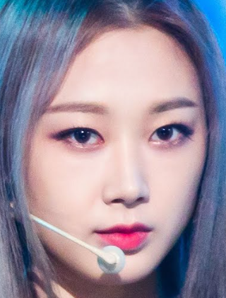 緑色の背景の前で口を少し開けた長い黒髪の女性の顔写真