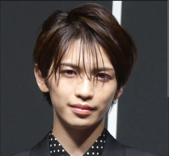 ダークカラーの衣装を着た人物が、前髪を下ろしたヘアスタイルで正面を見つめている上半身の写真。