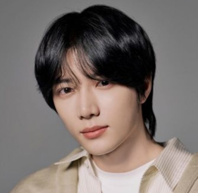 黒髪の人物がベージュ系の衣装を着て、グレー背景の前でやわらかい表情を見せているプロフィール写真。