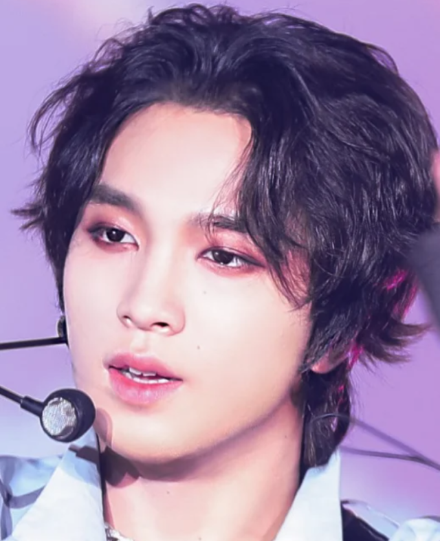 ステージ用マイクを付けた人物の顔写真。ふんわりした黒髪で、紫がかった背景の中、やや横を向いた表情を写している。