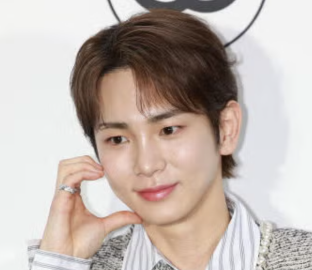 明るい背景の前で頬に手を添える人物のポートレート写真。茶色がかったセンターパートの髪型で、やわらかな表情を見せている。