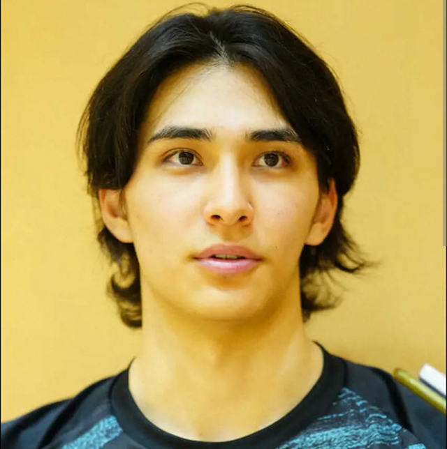 黒いスポーツウェアを着た人物の顔写真。センターパートの黒髪で、明るいベージュの背景の前でやや横を向いている。