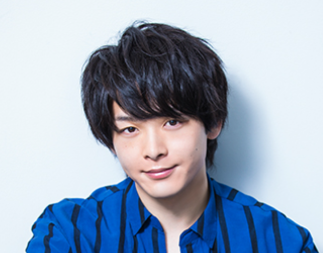 青いストライプ柄のシャツを着た人物のポートレート写真。黒髪のふんわりした髪型で、淡いグレーの背景の前でやわらかな表情を見せている。