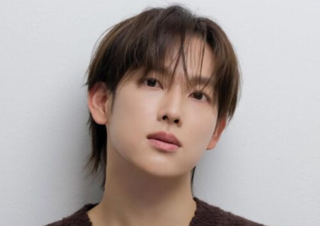 淡いグレーの背景の前で、やや首を傾けた人物のポートレート写真。茶色がかった前髪とやわらかな表情が印象的です。