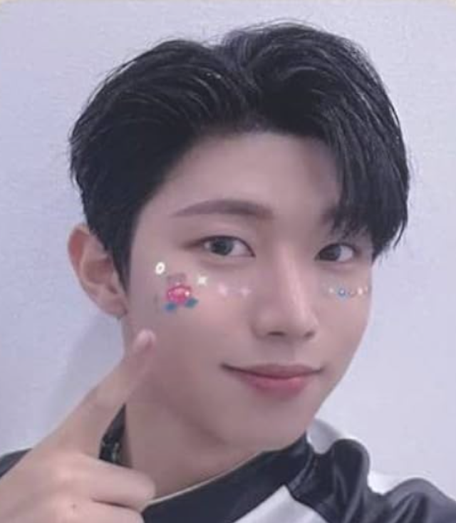 黒髪の若い男性が頬のシールを指差しながら、やわらかく微笑んでいる自撮り風の顔写真