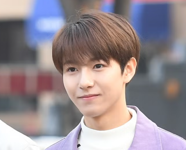 薄紫のジャケットを着た若い男性が、屋外でやわらかく微笑んでいる上半身写真