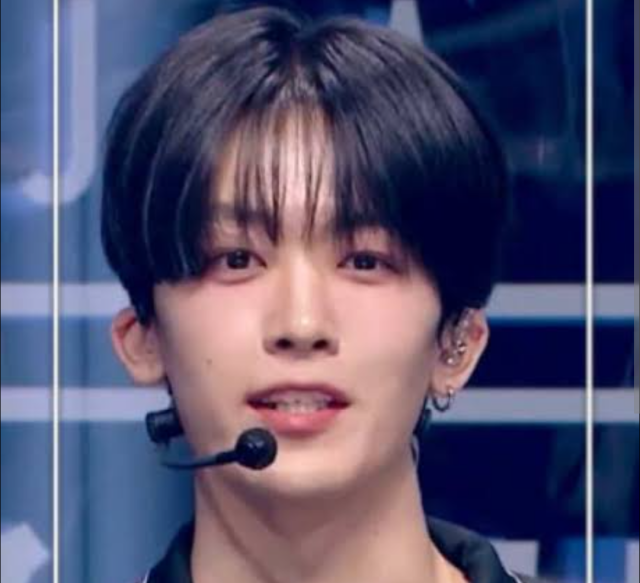 釼持吉成の正面アップ画像。黒髪センターパートでマイクを付け、ステージ上でこちらを見ている様子