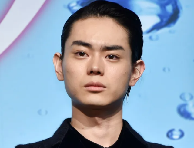 青い背景の前で、黒い衣装を着た菅田将暉が正面を向いているバストアップ画像。きりっとした目元と整った輪郭が印象的です。