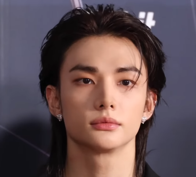 黒い衣装を着たヒョンジンが、暗めの背景の前で正面を向いて写っているバストアップ画像。印象的な目元と整った鼻筋、落ち着いた表情が目を引きます。