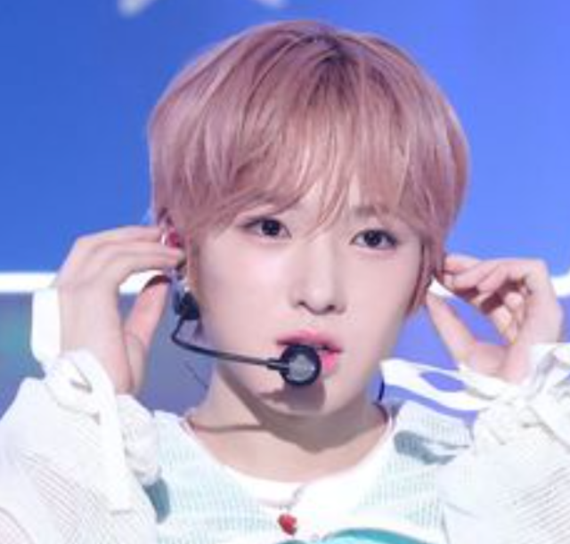 ピンクベージュの髪色で白い衣装を着たサクヤが、ヘッドセットマイクを付けて両手でイヤモニを調整している上半身画像