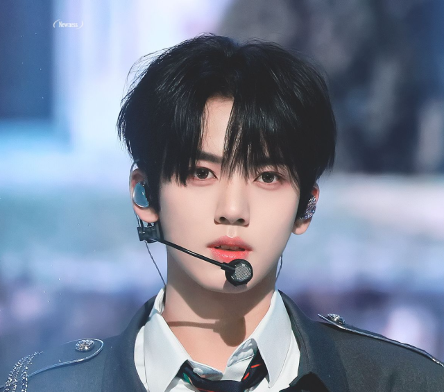 黒髪でステージ衣装を着た人物が、ヘッドセットマイクとイヤモニを付けて正面を見つめている上半身画像