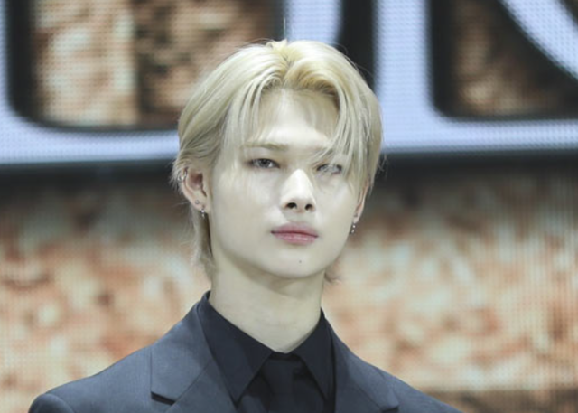 黒いスーツ姿で登壇するニキの上半身画像。金髪ヘアと切れ長の目元が印象的なショット