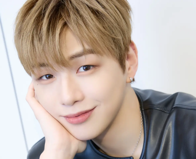 金髪の若い男性が頬杖をつき、やわらかく微笑んでいる顔アップ写真。すっきりした目元と鼻筋、明るく親しみやすい表情が印象的。